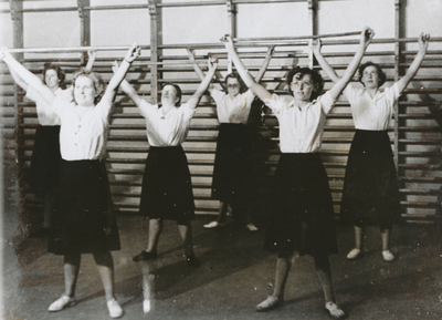 876913 Afbeelding van enkele jonge vrouwen op een gymnastiekles tijdens hun opleiding tot sociaal werkster bij de ...